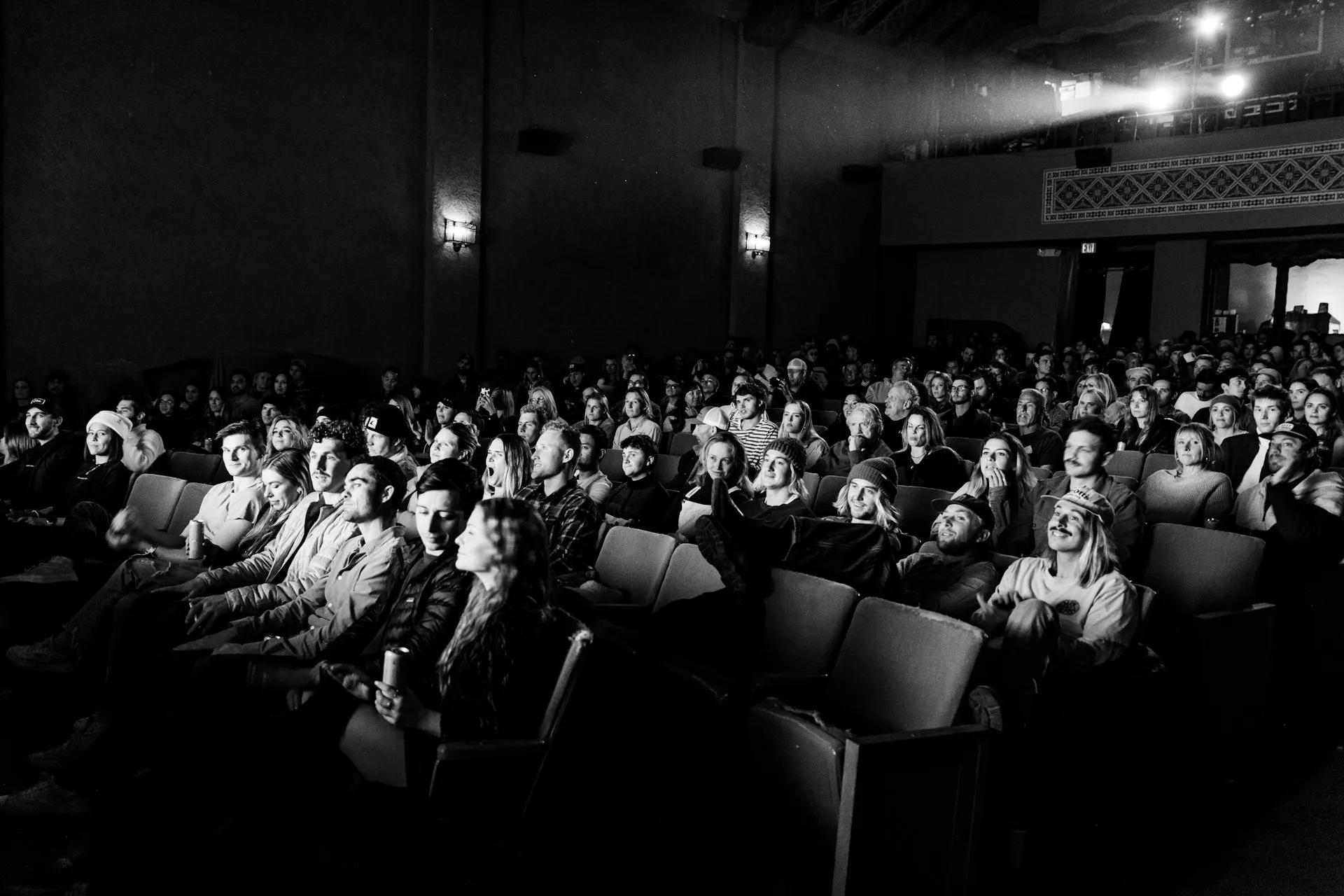 Público llenando una sala de cine, en blanco y negro, con el haz del proyector al fondo